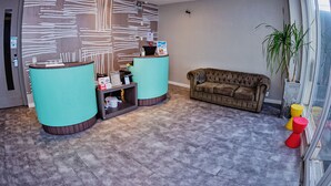 A reception area with two teal counters, a brown sofa, and a potted plant by a window. - B Hotel (Salvador)