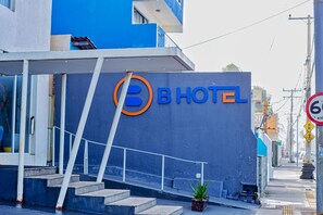 A modern hotel with a prominent 'B HOTEL' sign, a staircase leading to the entrance, and a small potted plant on the ground. - B Hotel (Salvador)