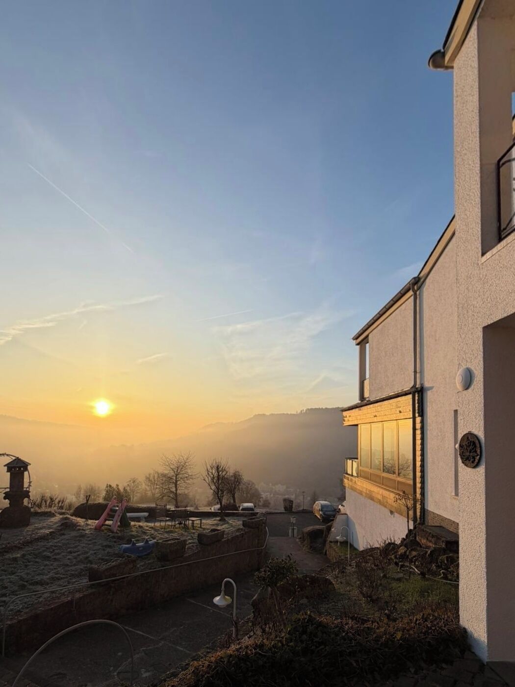 Ein Gebäude mit modernem Design, einem gepflasterten Innenhof und Blick auf einen Hügellandstrum gegen den Sonnenuntergang.