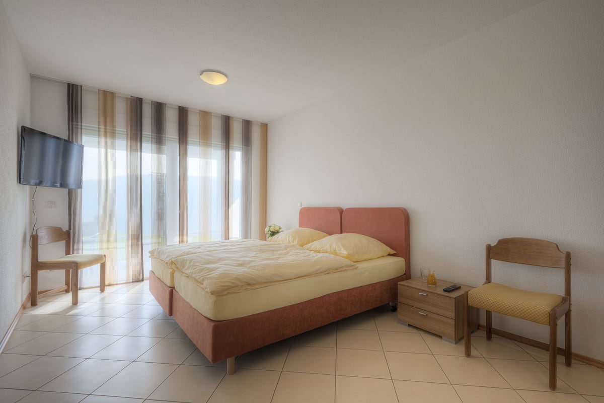 Un dormitorio con una cama, una silla, un televisor y una mesita de noche.