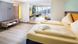 A modern hotel room with a bed, seating area, and a view of mountains. - Waldhotel Sonnenberg (Bollendorf)