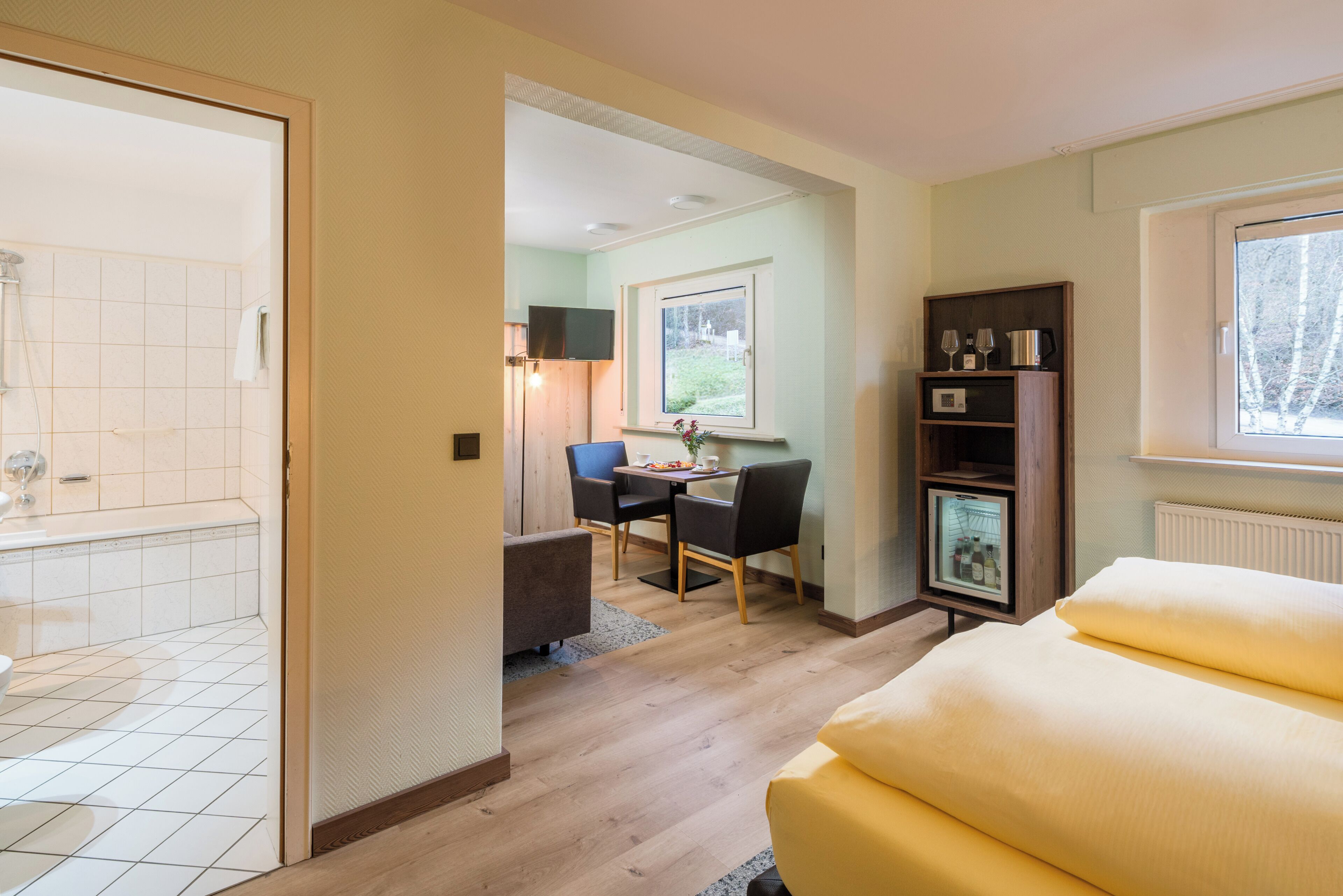 A hotel room with a bathroom, a dining area, a sofa, and a bookshelf.