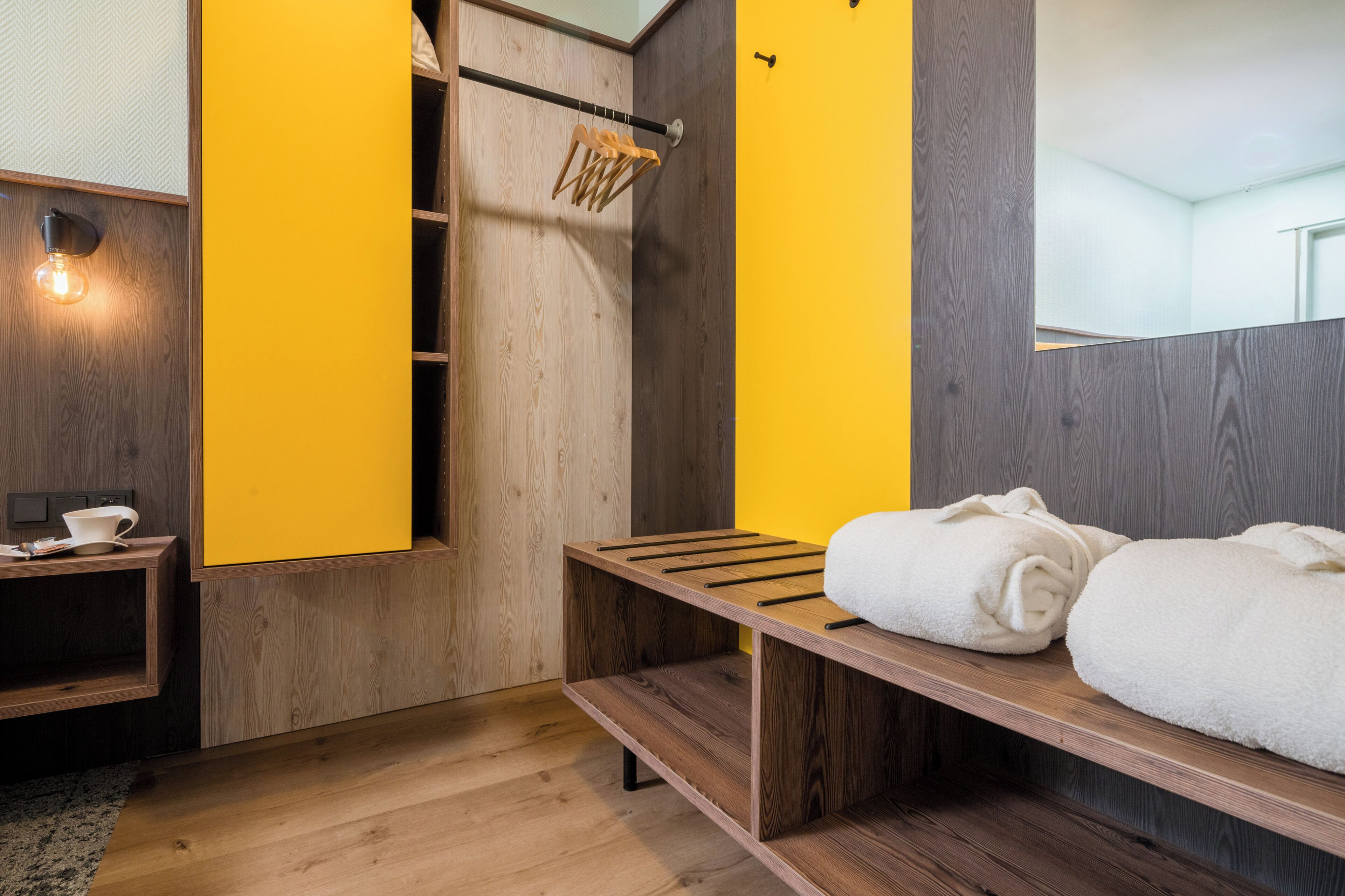 Ein modernes Badezimmer mit Holzsäcken, einer Sitzbank mit Handtüchern, einem Kleiderständer und einer Leuchte.