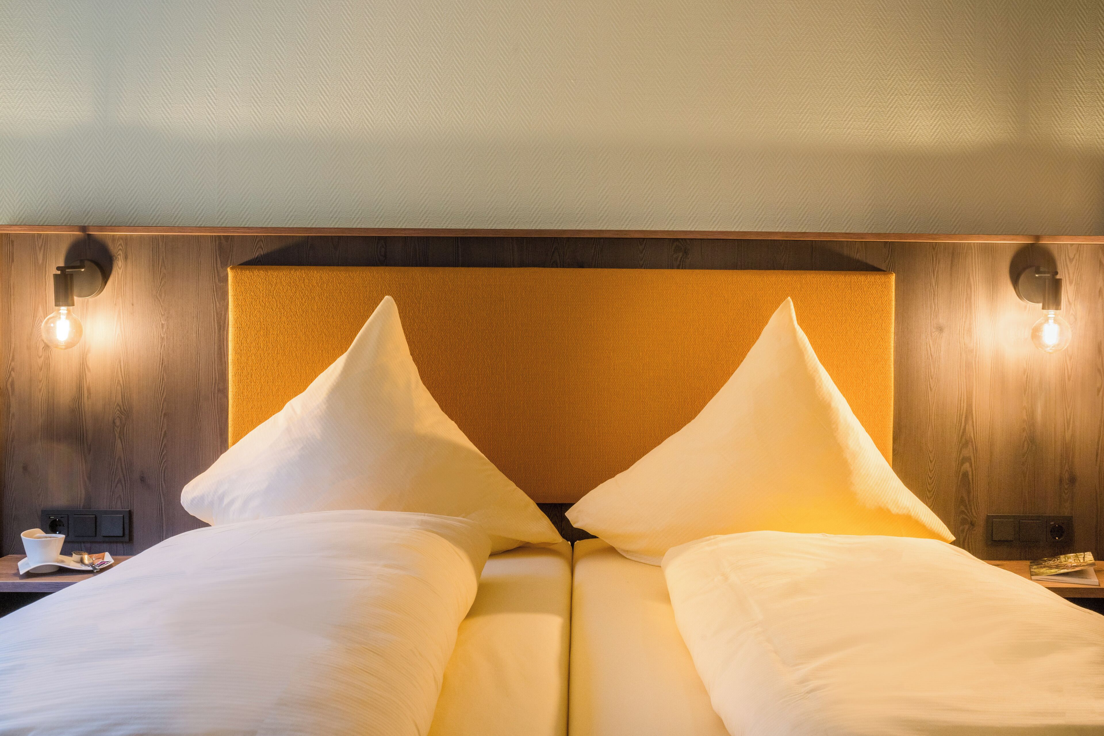 Ein Hotelzimmer mit einem hölzernen Kopfteil, zwei weißen Kissen und einem Nachttisch mit einer Lampe.