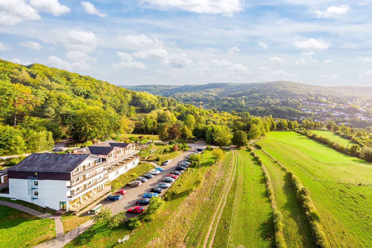 Un hotel con estacionamiento, un edificio de varios pisos y vistas a un paisaje verde con campos y colinas.