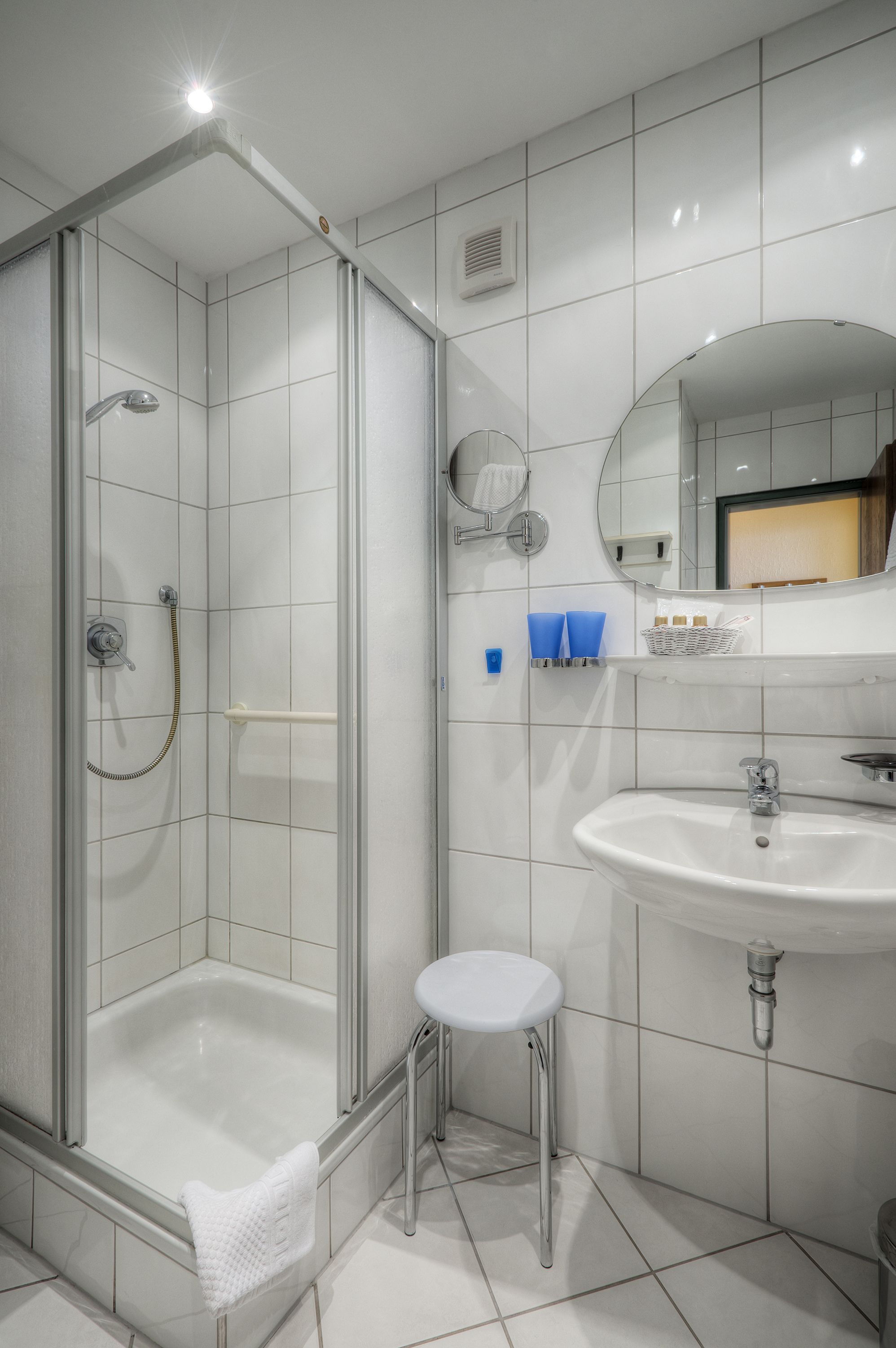 A modern bathroom with a glass-enclosed shower, a white sink, and a small stool.