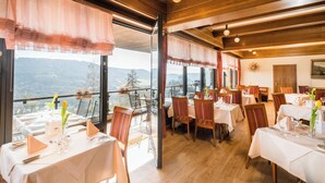 A restaurant with multiple tables, chairs, and a view of the mountains. - Waldhotel Sonnenberg (Bollendorf)