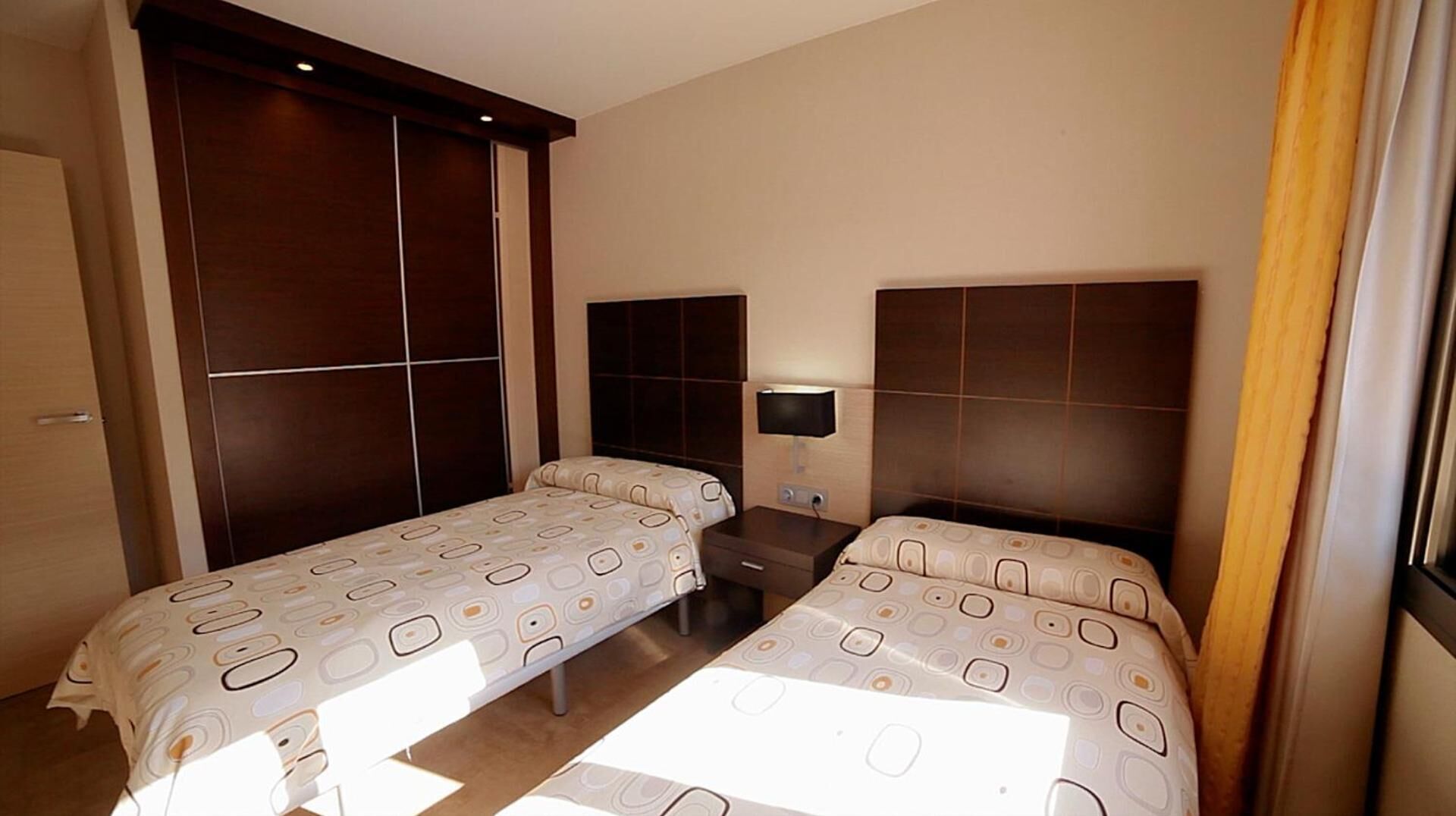 A hotel room with two beds, a large wardrobe, a bedside table, and a wall-mounted TV.