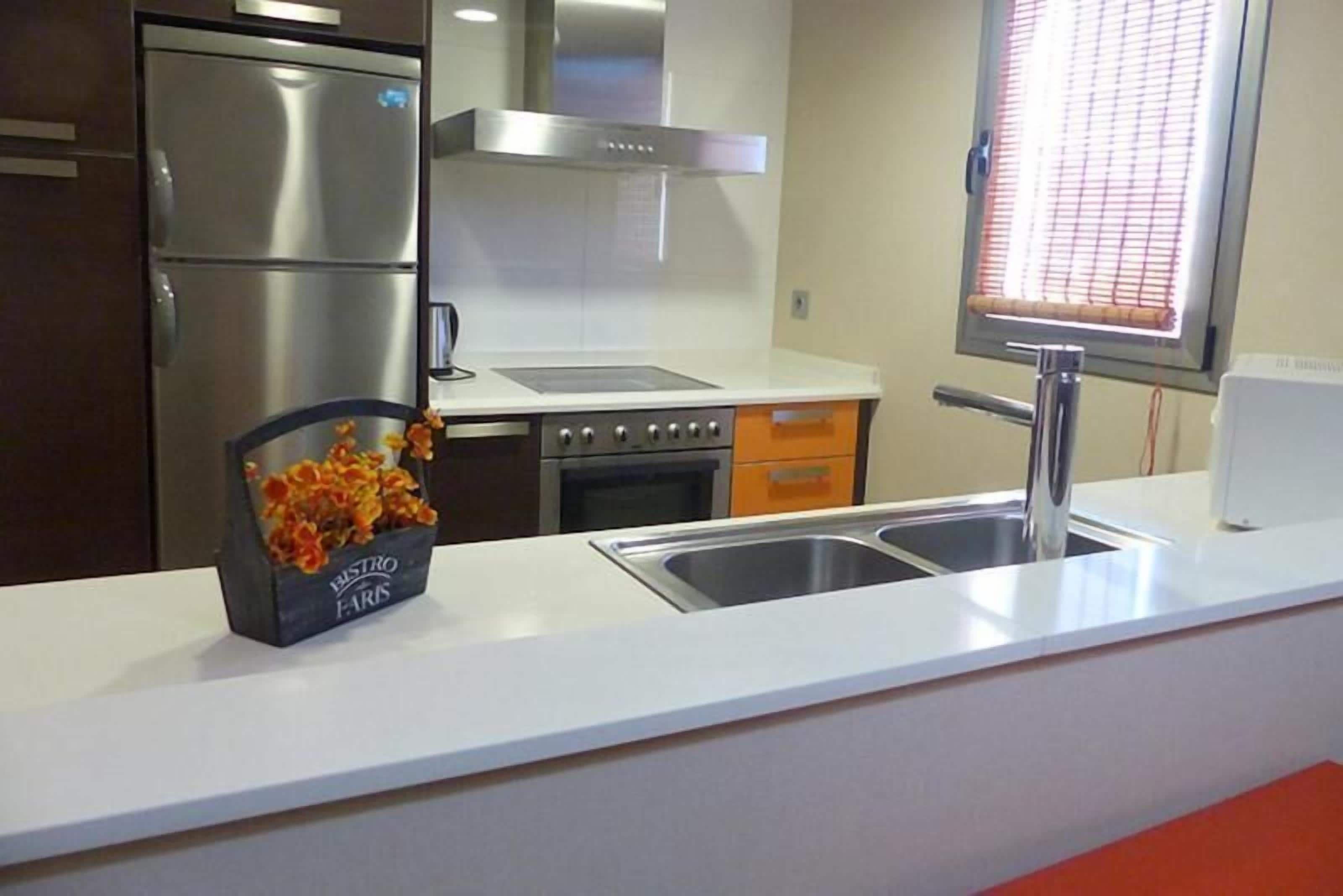 A modern kitchen with stainless steel appliances, a white countertop, and a window with blinds.