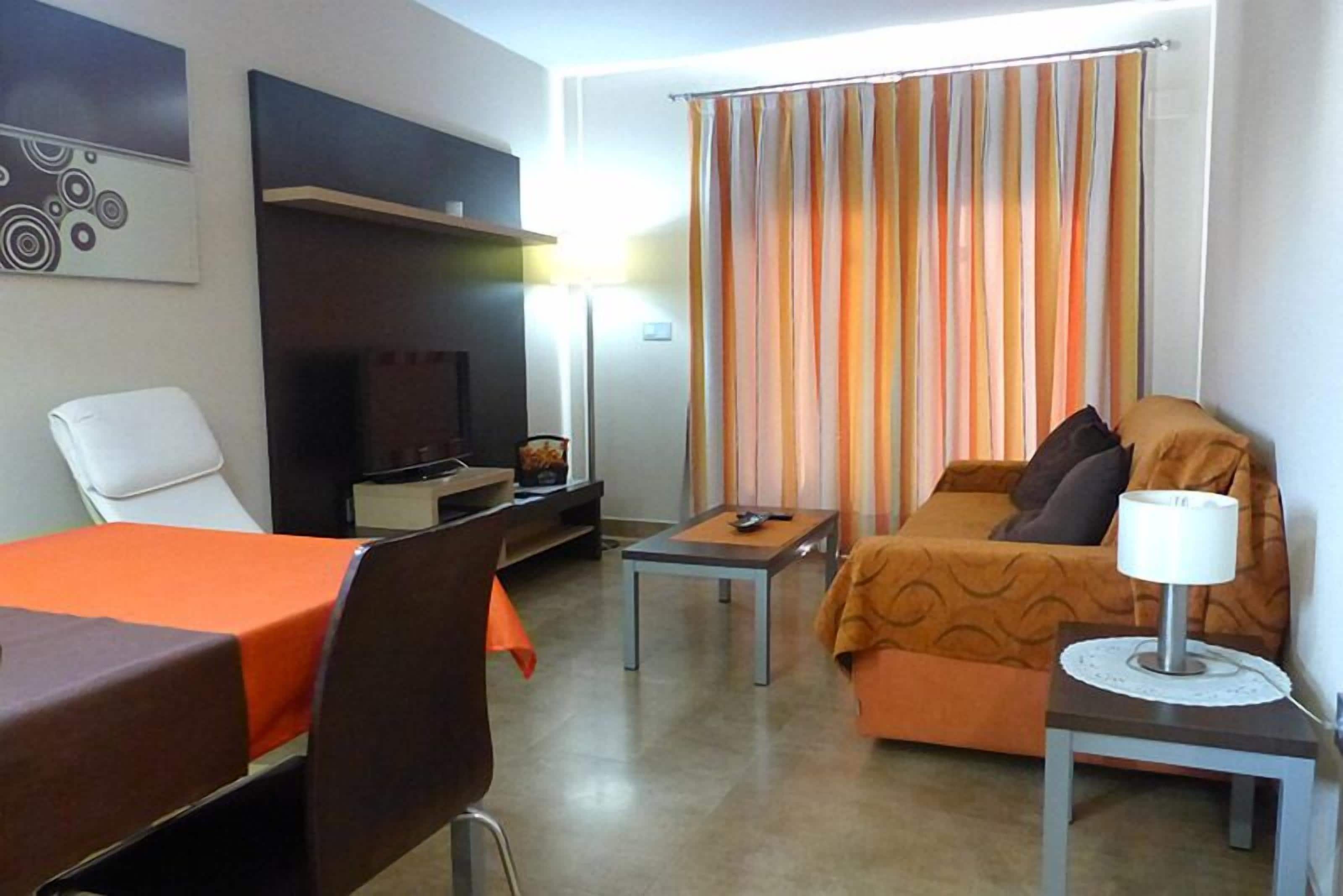 A hotel room with a bed, a desk, a chair, a TV, and a window with curtains.