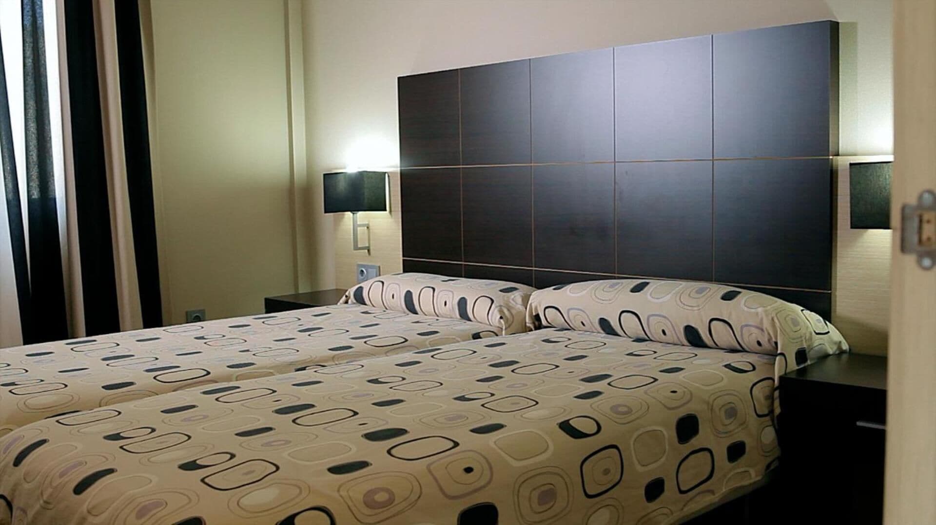 A hotel room with a large bed, two bedside tables, a flat-screen TV, and a dark headboard.