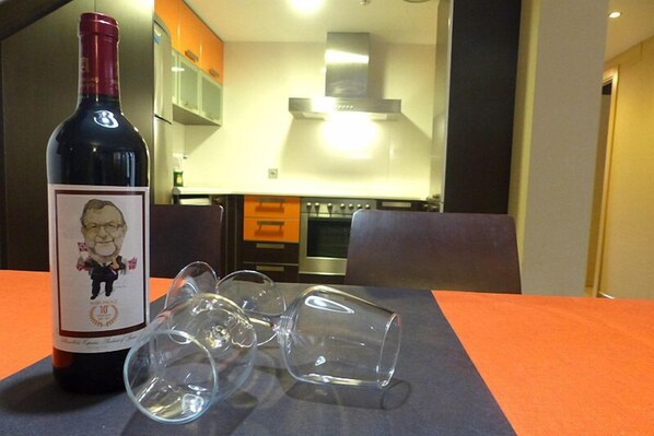 Una botella de vino y copas de vino vacías sobre una mesa en una cocina moderna con armarios color naranja y electrodomésticos de acero inoxidable.