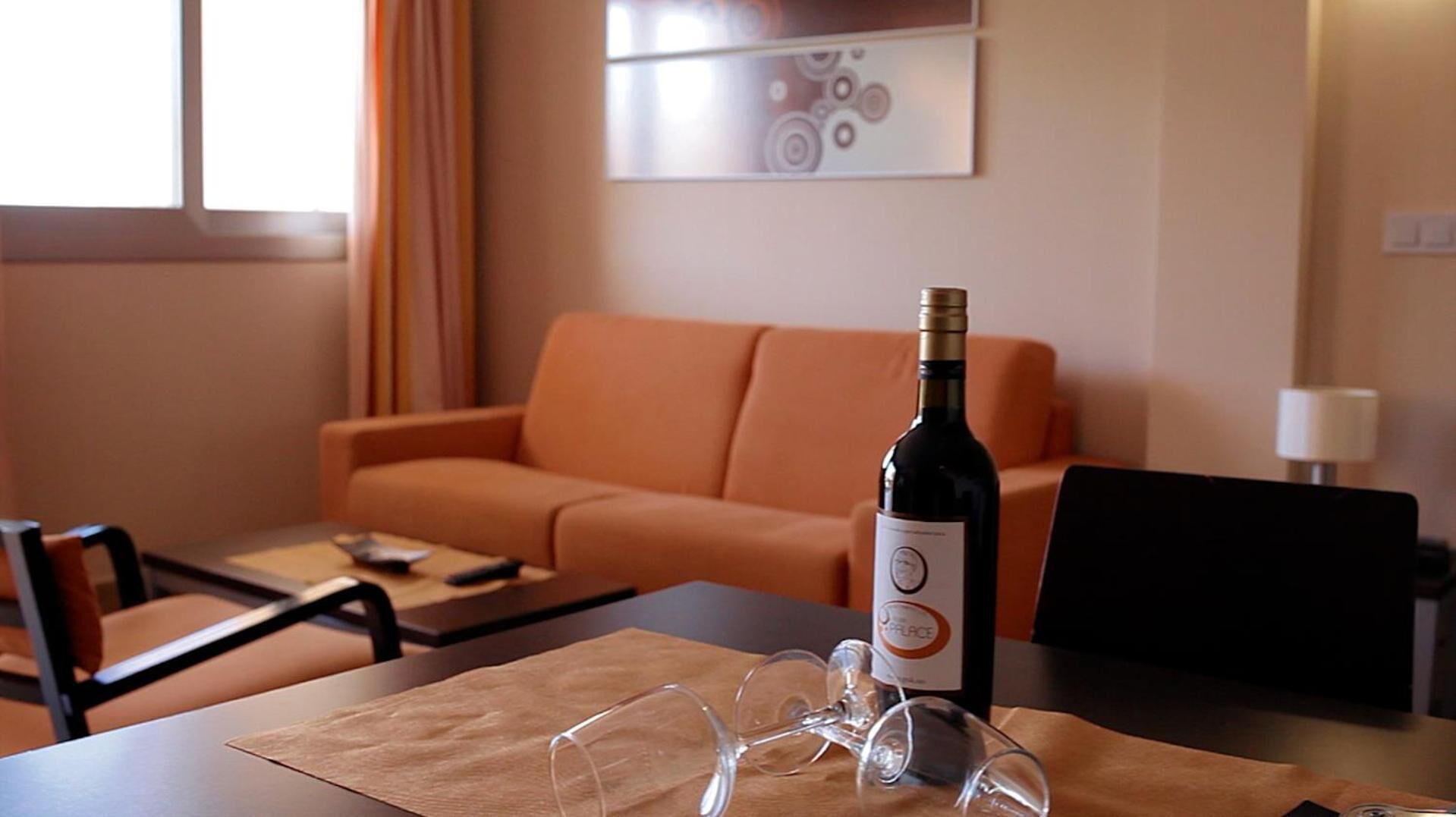 A hotel room with a wooden table, a bottle of wine, and wine glasses.
