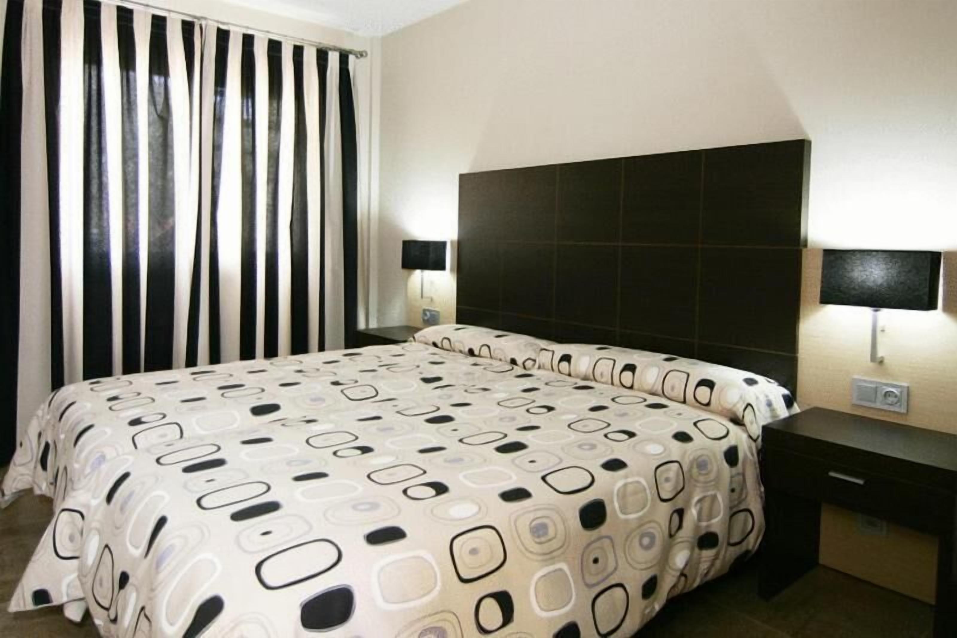 Une chambre d’hôtel avec un lit, une table de chevet, une lampe et une fenêtre avec des rideaux.