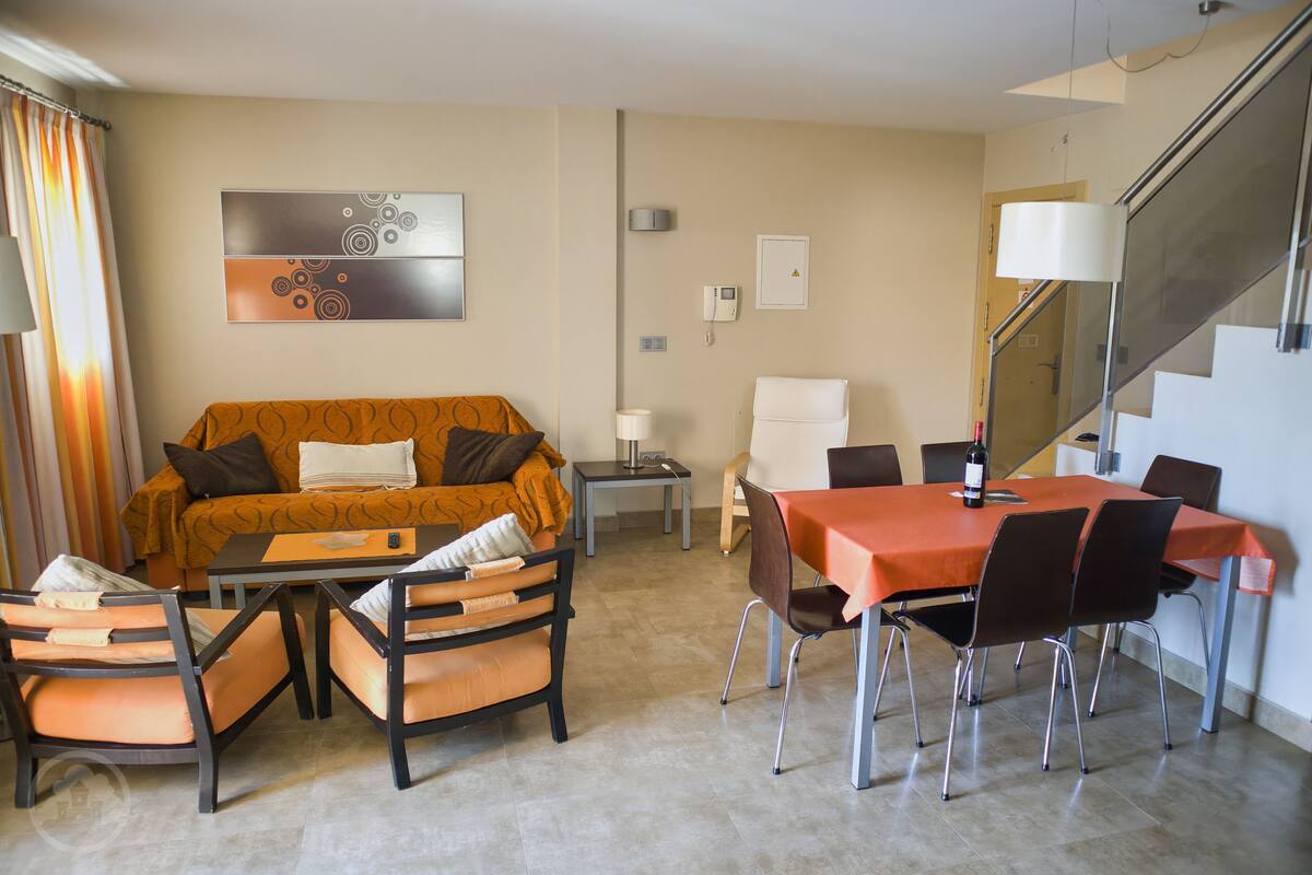 A modern hotel room with a sofa, dining table, chairs, and a staircase.