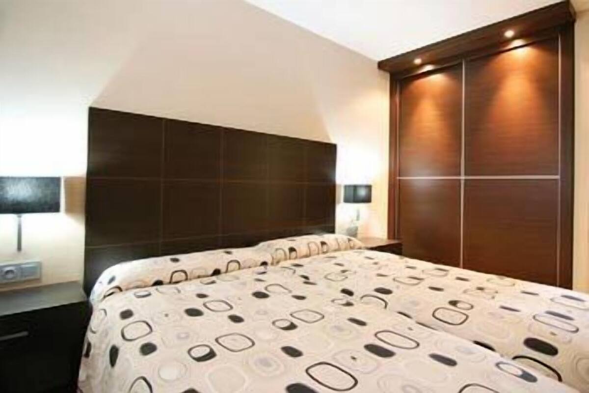A bedroom with a large bed, dark headboard, bedside table, lamp, and a wardrobe.
