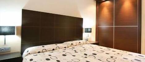 A bedroom with a large bed, dark headboard, bedside table, lamp, and a wardrobe.