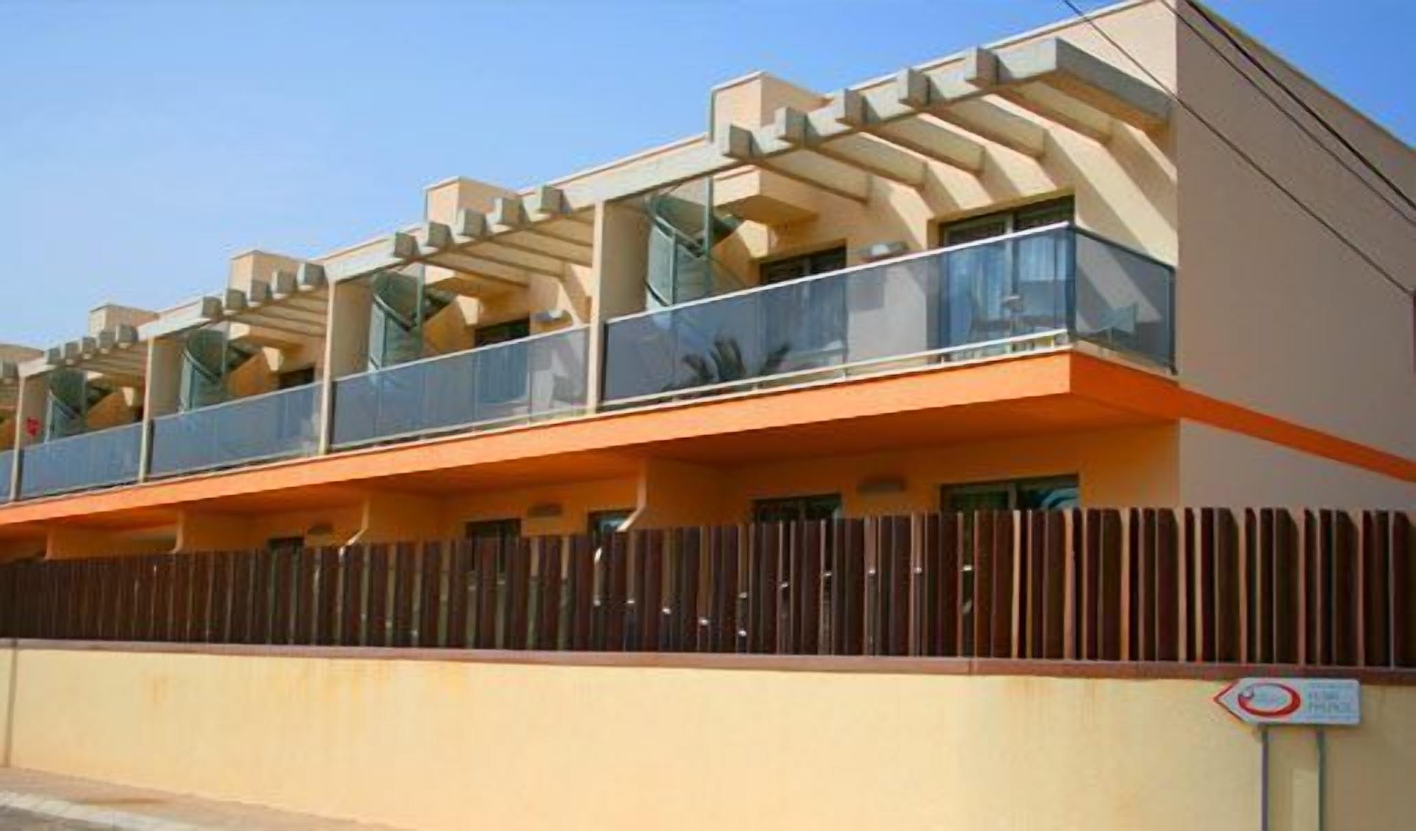 Un edificio moderno de varios pisos con balcones y una valla de madera.