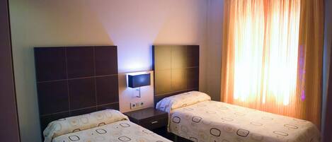 A hotel room with two beds, a TV, and a window with curtains.