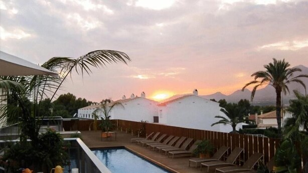 Un área de piscina en la azotea con sillones de descanso y vistas al atardecer.