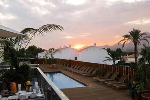 Un área de piscina en la azotea con sillones de descanso y vistas al atardecer.