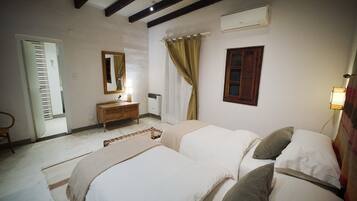 A bedroom with two beds, a wooden dresser, a mirror, a window with curtains, and an air conditioning unit.