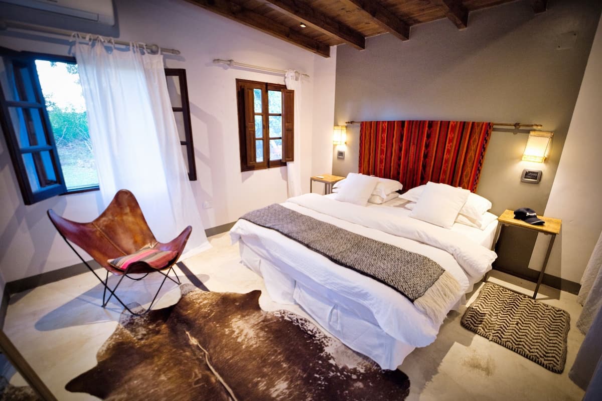 A bedroom with a large bed, a chair, a rug, and a window with curtains.