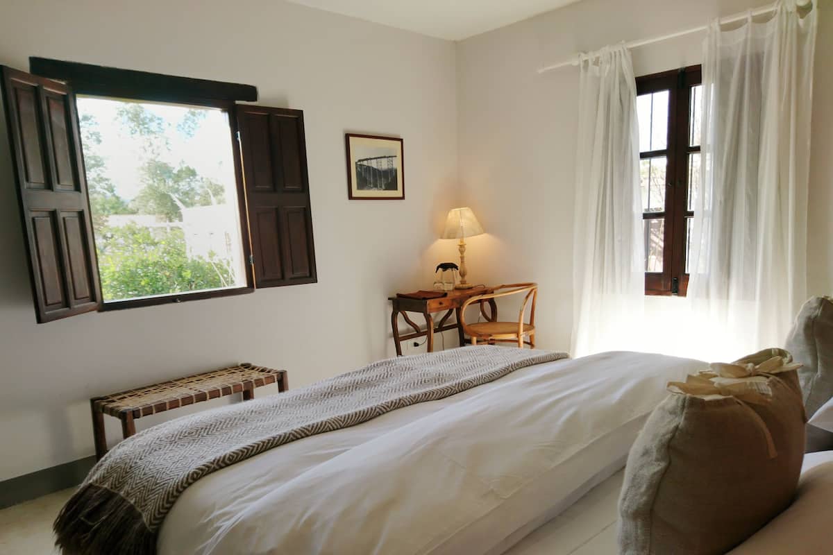 A bedroom with a bed, a desk, a chair, a lamp, and a window with curtains.