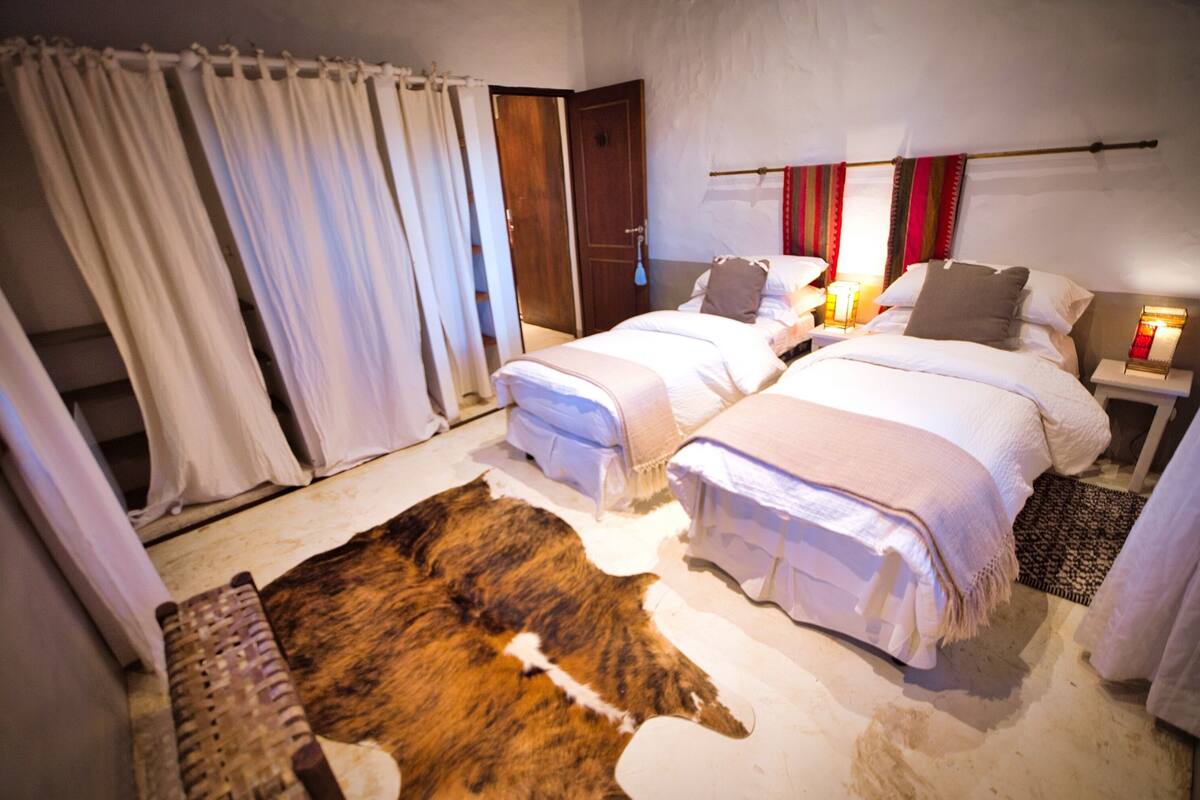 A room with two beds, a large fur rug, and a wooden door.