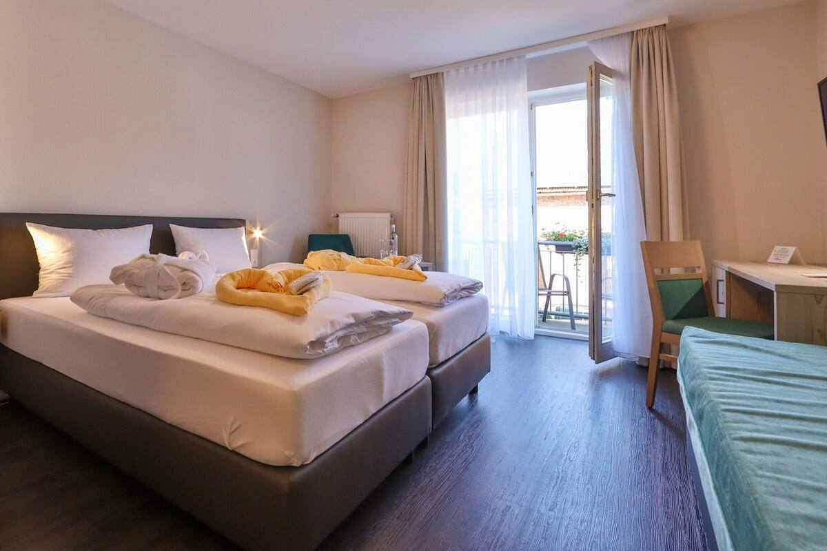 Ein Hotelzimmer mit einem großen Bett, einem Schreibtisch und einem Stuhl. Ein Fenster mit Vorhängen bietet einen Blick nach draußen.