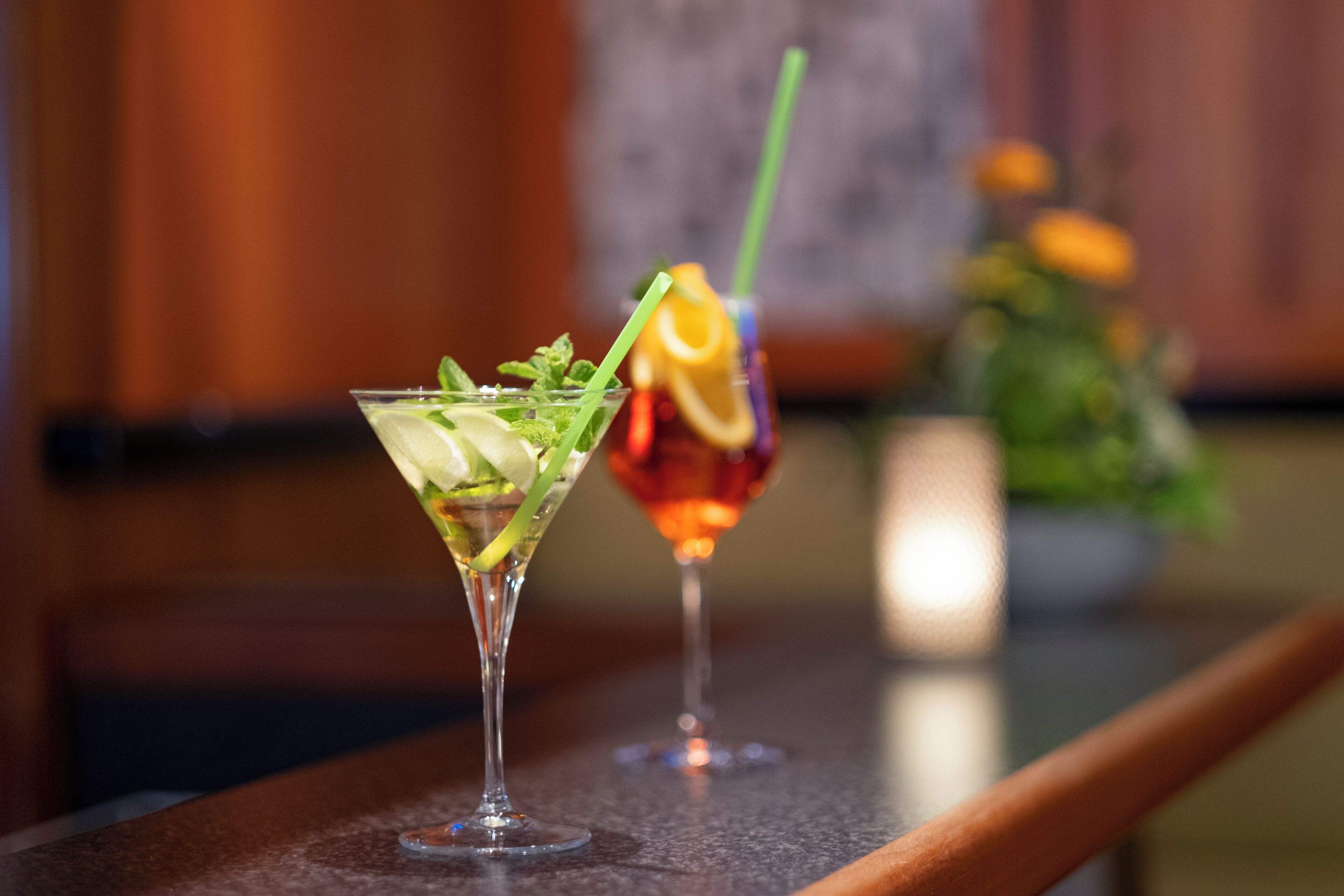 Two cocktails on a bar counter with a blurred background.