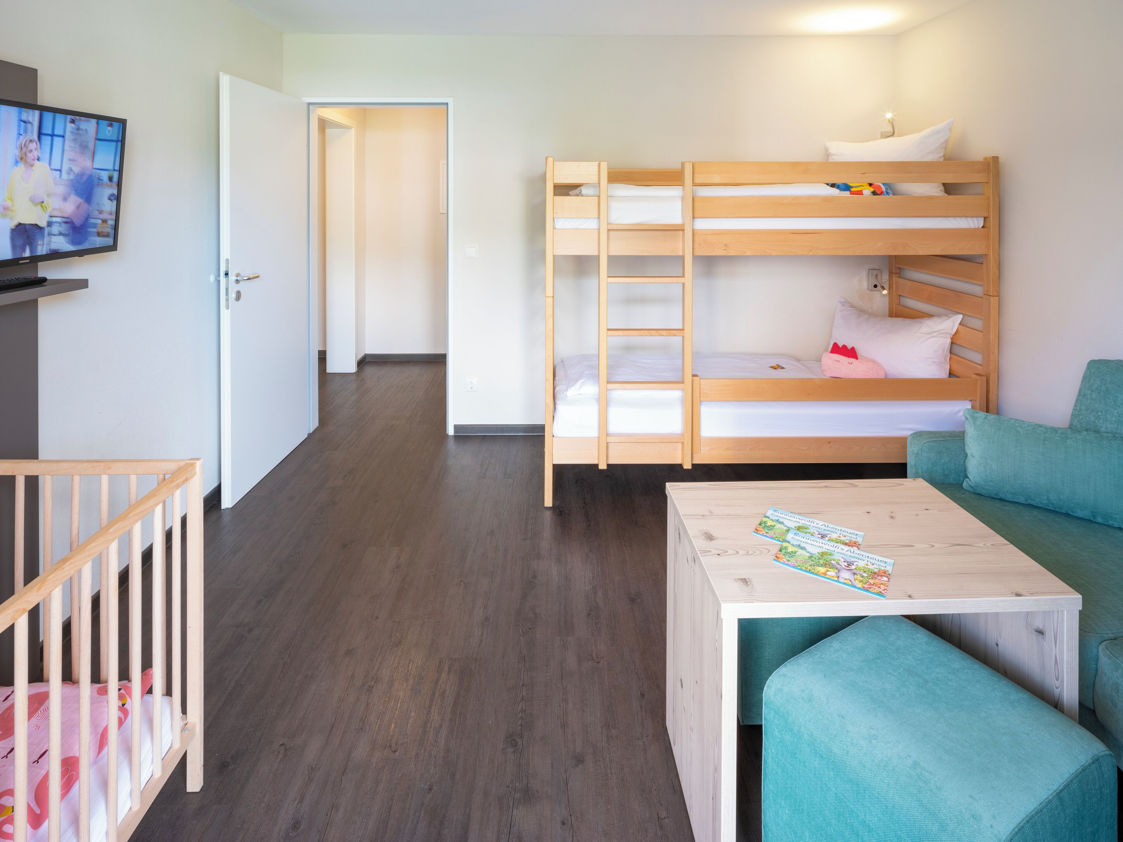 Una habitación con una cama litera, una mesita con revistas, un sofá verde y un televisor en la pared.