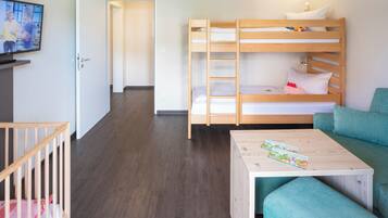 Una habitación con una cama litera, una mesita con revistas, un sofá verde y un televisor en la pared.