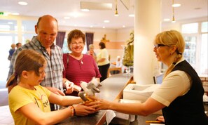 Een groep mensen bij een balie, mogelijk in een restaurant of café, waarbij een kind een speeltje krijgt van een volwassene.