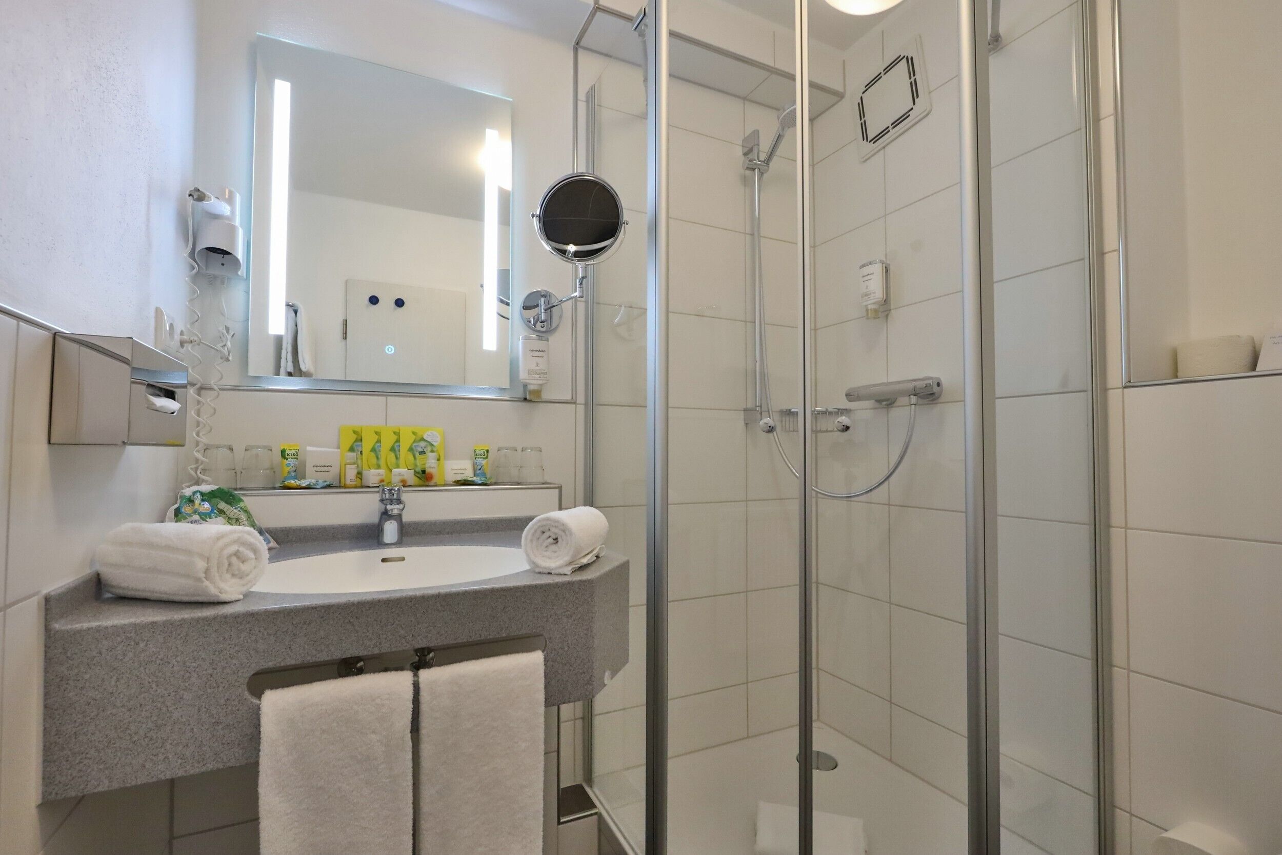 A modern bathroom with a glass-enclosed shower, a sink with a mirror, and toiletries on the counter.