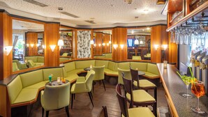 Een restaurant met groene banken, houten tafels en een bar.