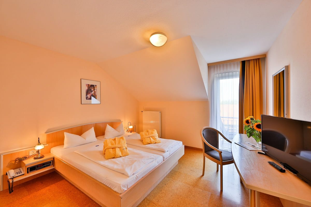 Ein Hotelzimmer mit zwei Betten, einem Schreibtisch, einem Stuhl, einem Fernseher und einem Fenster mit Vorhängen.