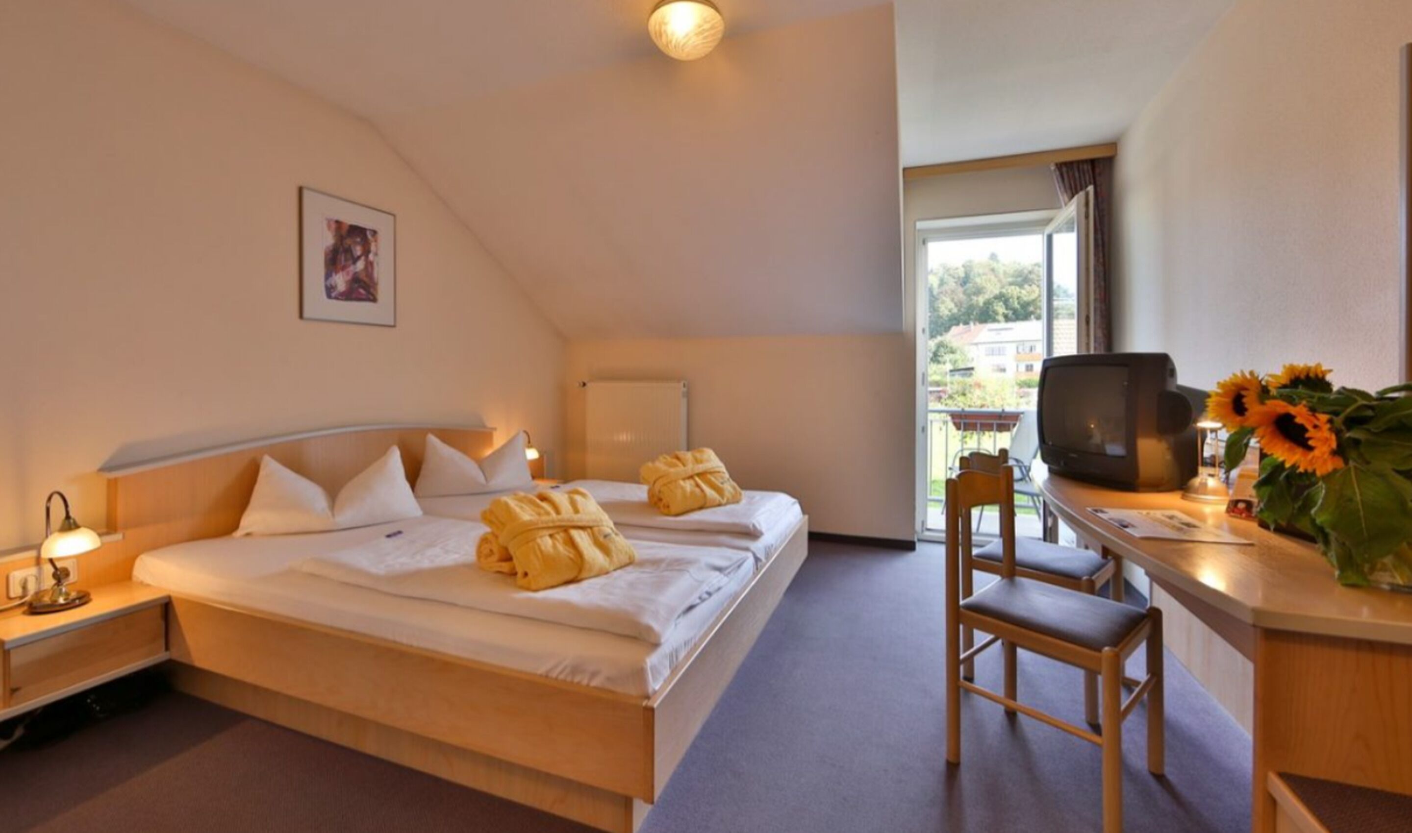 A hotel room with a bed, a desk with a television, a chair, and a window with a view of the outside.