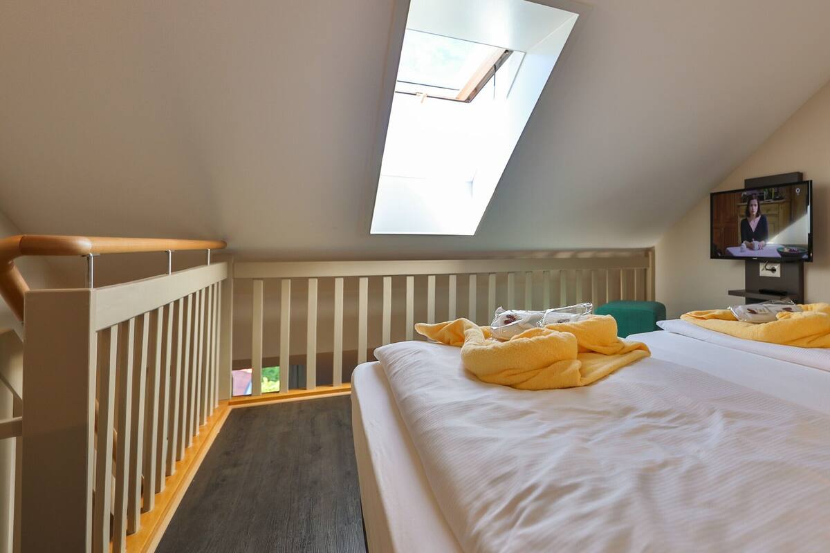 Ein Hotelzimmer mit Dachfenster, einem Bett mit gelben Handtüchern, einem Fernseher und Blick ins Freie.