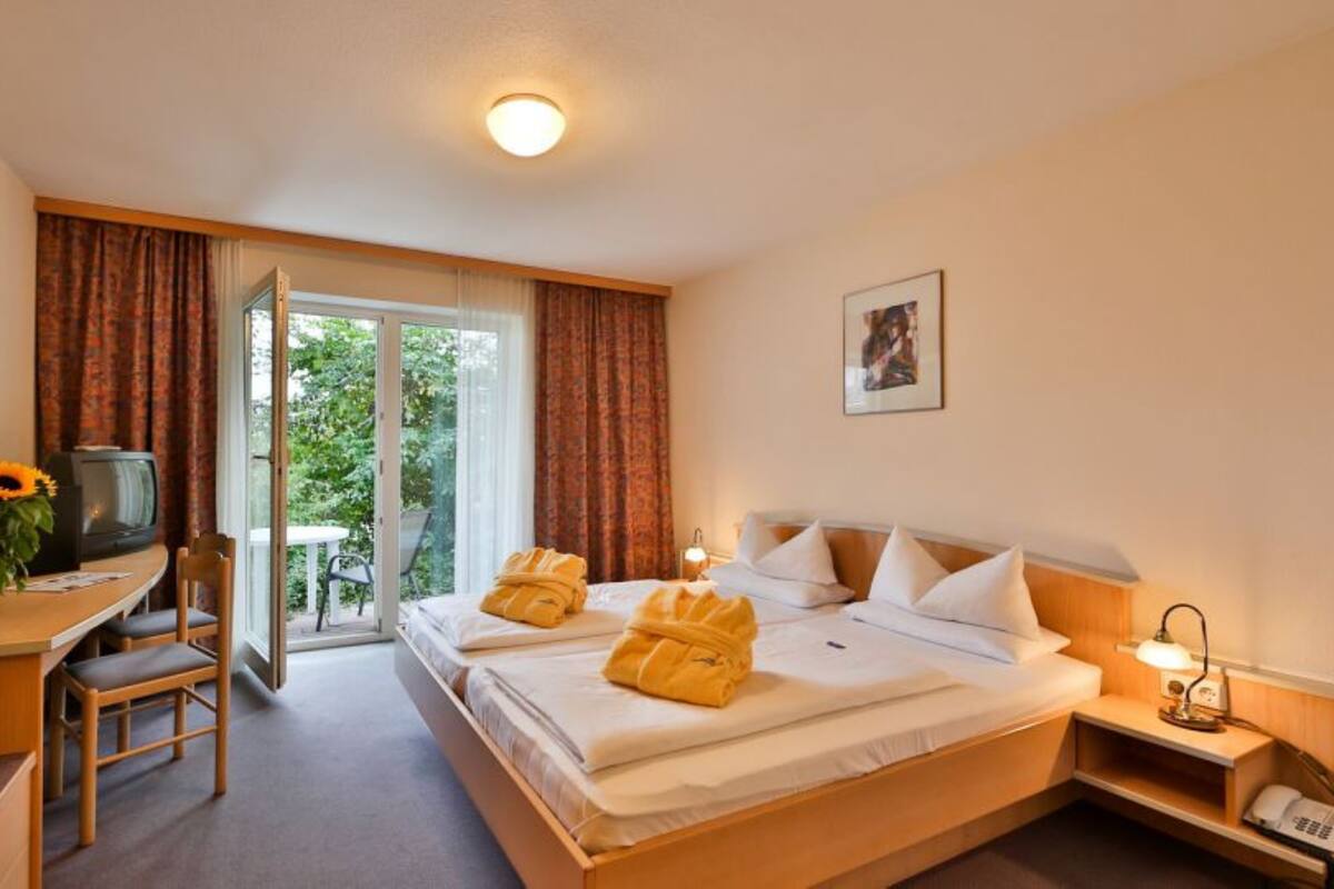 Ein Hotelzimmer mit Bett, Schreibtisch, Stuhl, Fernseher und Blick ins Freie.
