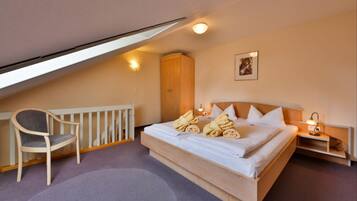 A bedroom with a bed, a chair, a wardrobe, and a small table with a lamp.