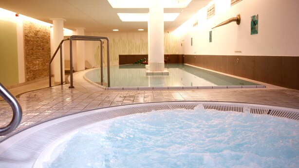 Een deel met een jacuzzi, zwembad, betegelde vloer en een leuning.