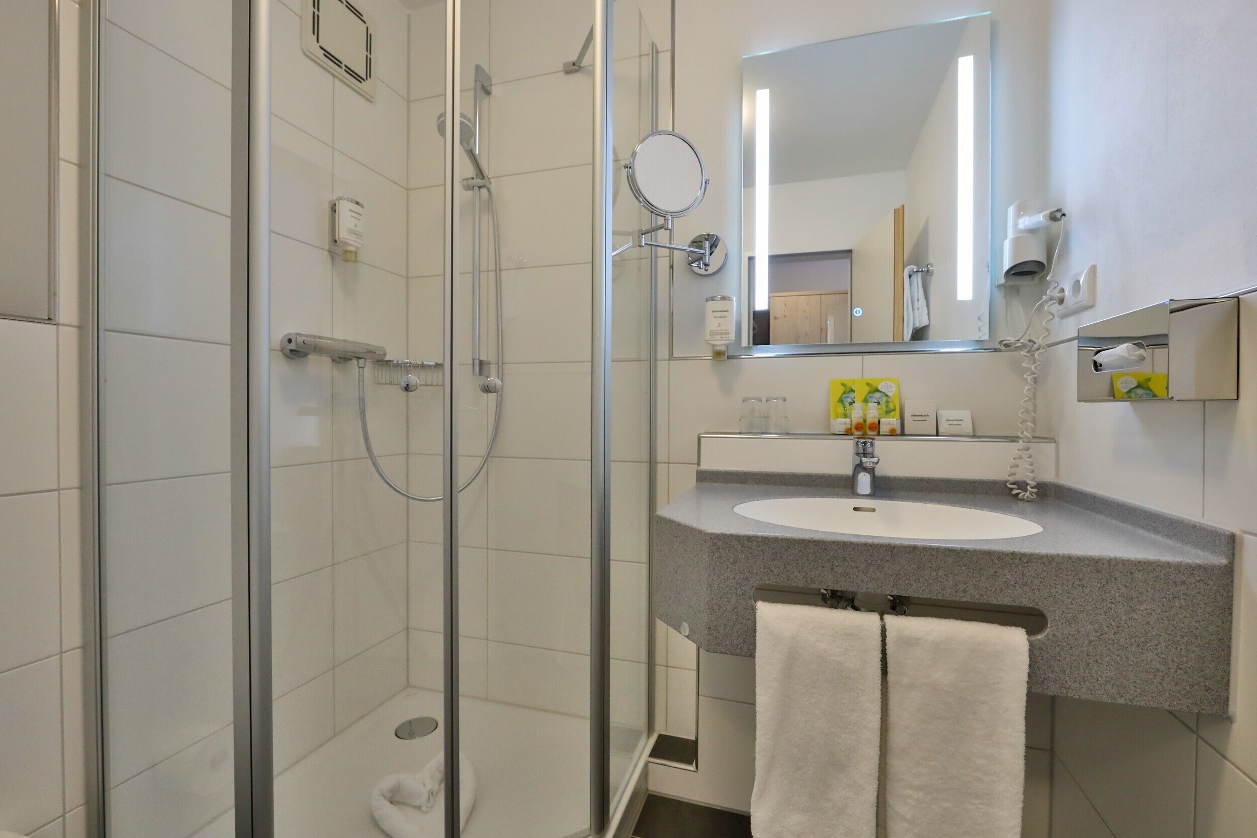 Un baño moderno con ducha envuelta en cristal, un lavamanos con espejo y un perchero para toallas.