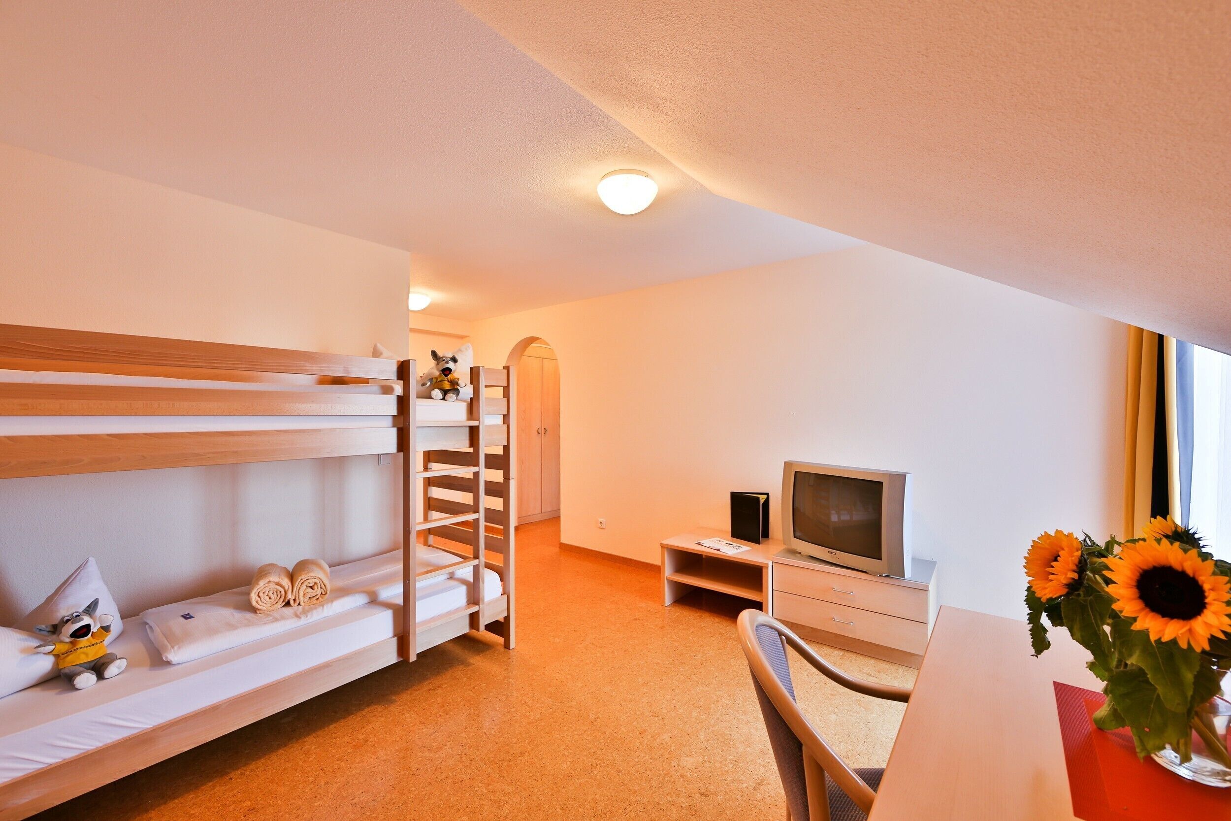 A hotel room with bunk beds, a TV, a desk, and a vase with sunflowers.