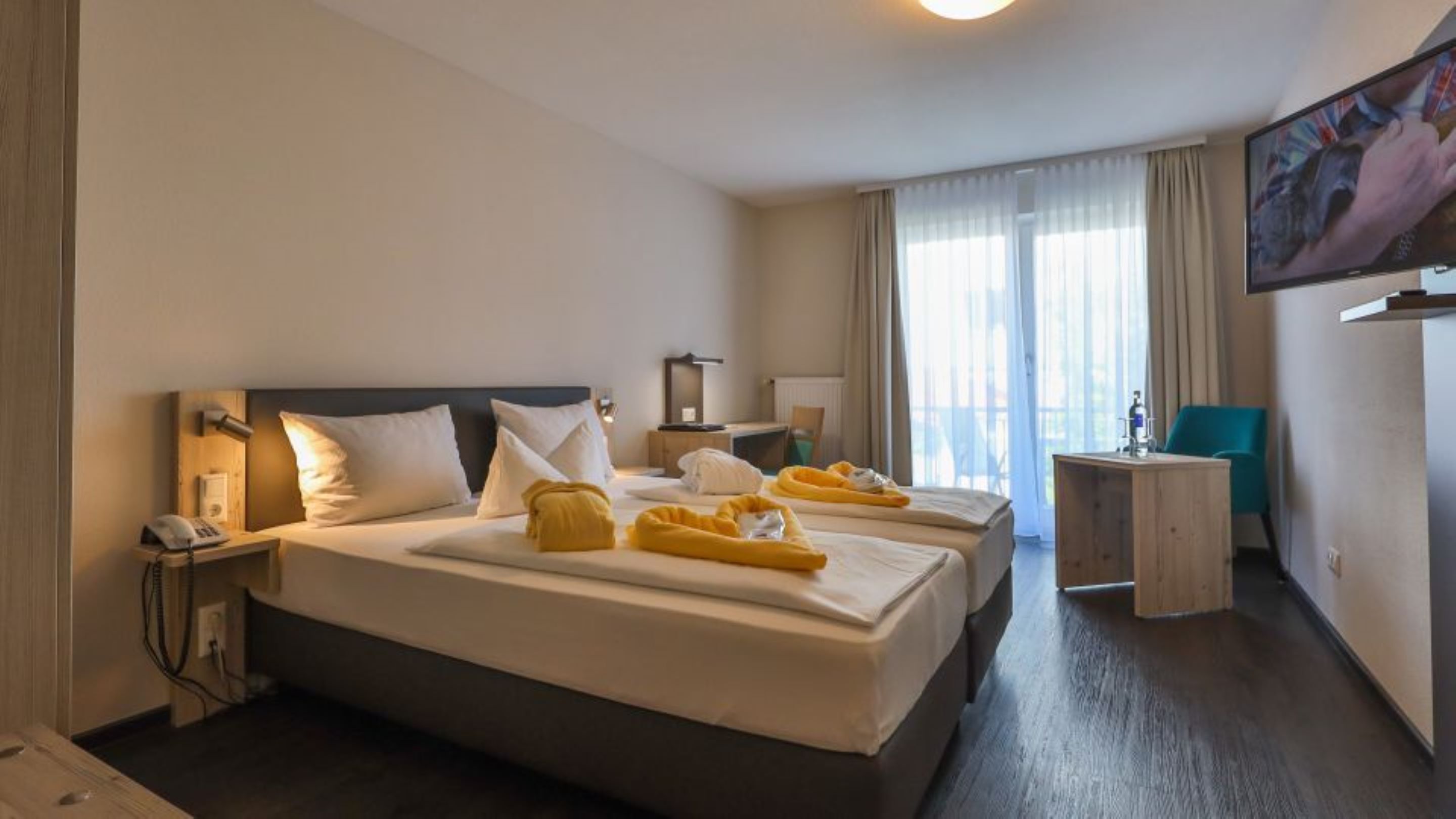 A hotel room with two beds, a desk, a chair, a TV, and a window with curtains.