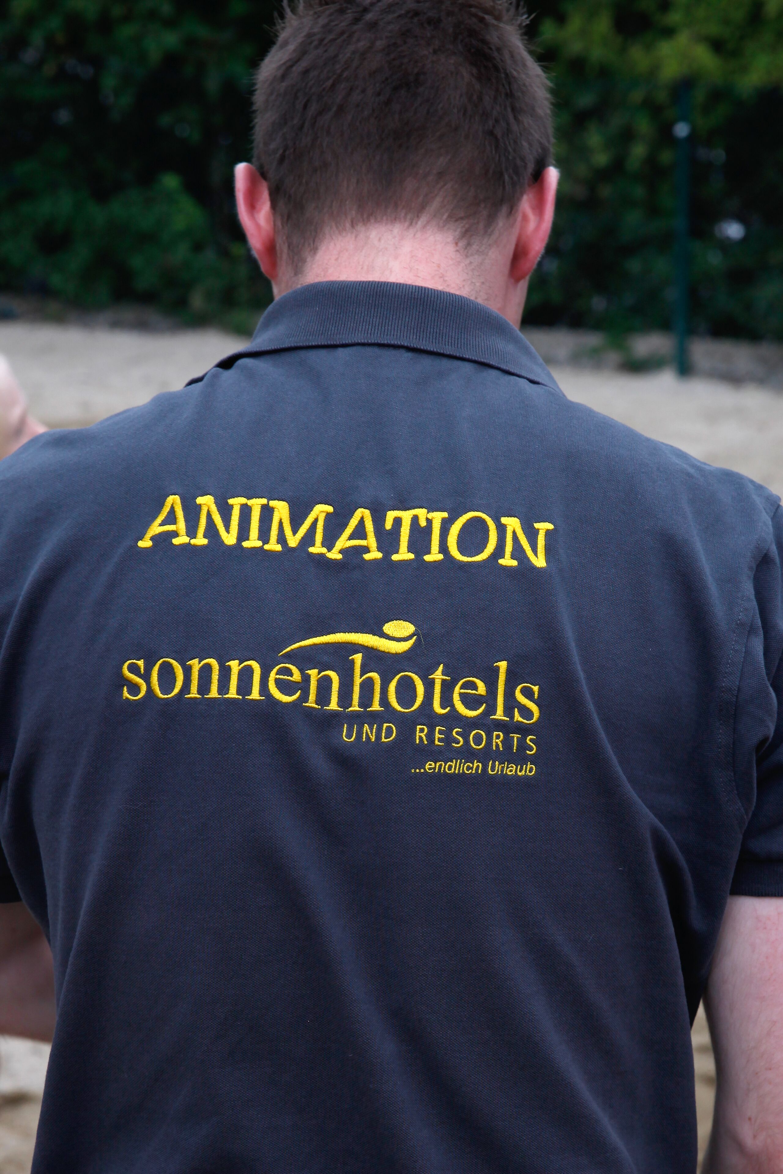 Una persona con una camisa azul oscuro que tiene el texto "ANIMATION" y "sonnenhotels UND RESORTS" en la parte posterior.