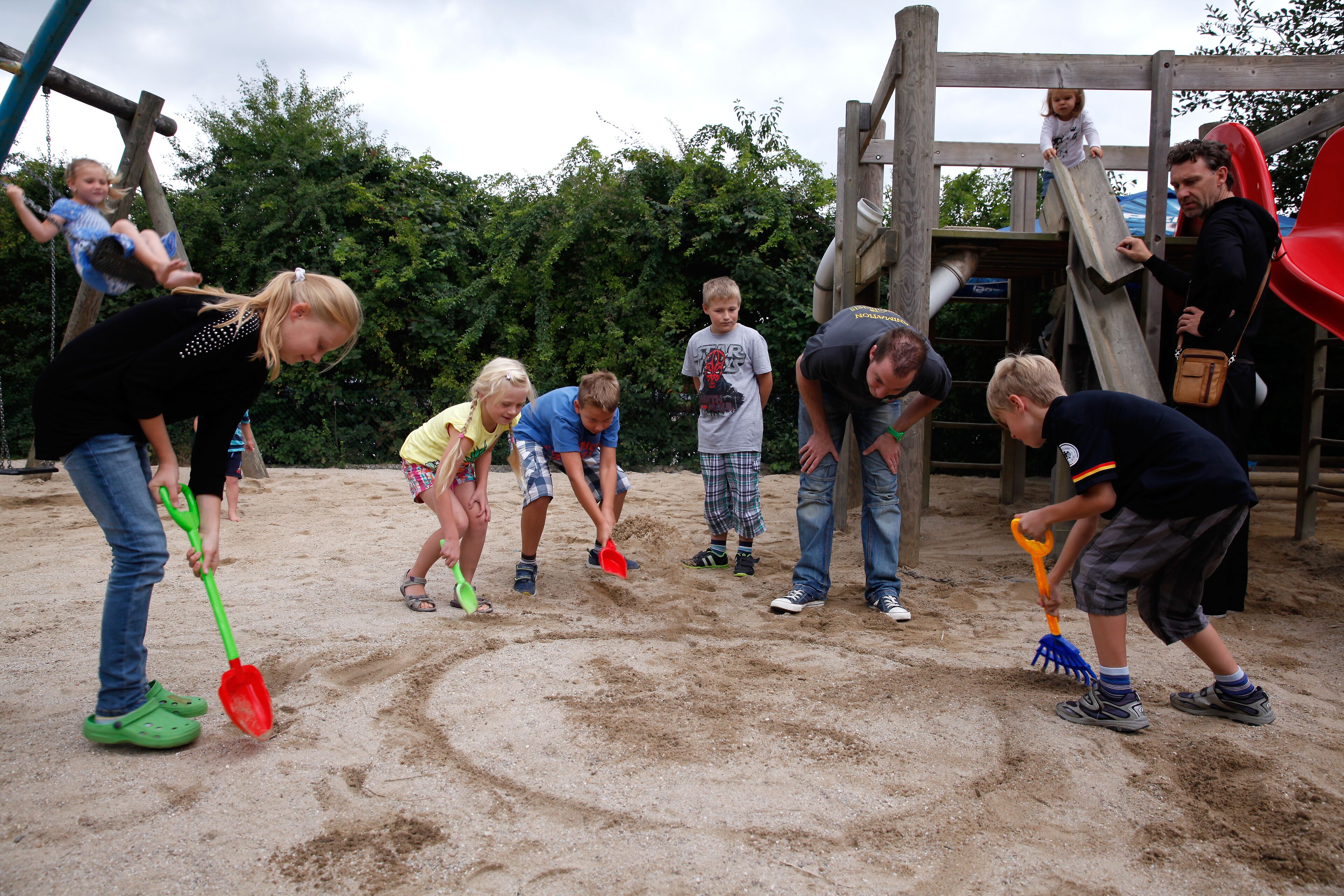 A group of children playing in a sandy area with playground equipment in the background.