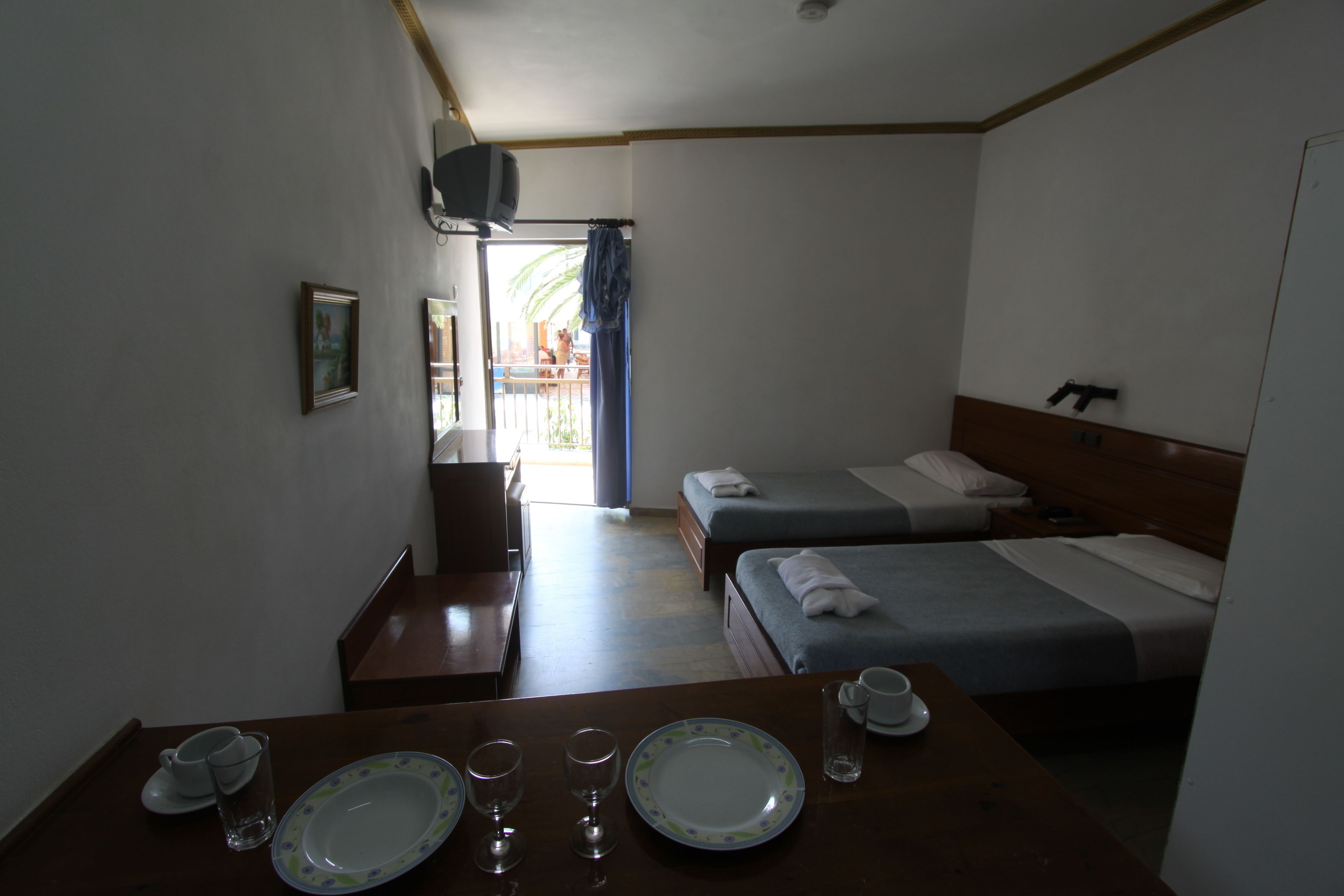 Ein Hotelzimmer mit zwei Betten, einem kleinen Tisch mit Tellern und Gläsern, einem Fernseher und Blick auf den Balkon.
