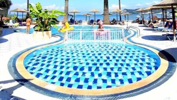 A pool area with a thatched roof, palm trees, and lounge chairs. - Maria' s Beach Apartments (Corfu)