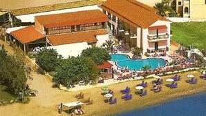 An aerial view of a resort with a swimming pool, beach chairs, and a building with a red roof. - Maria' s Beach Apartments (Corfu)